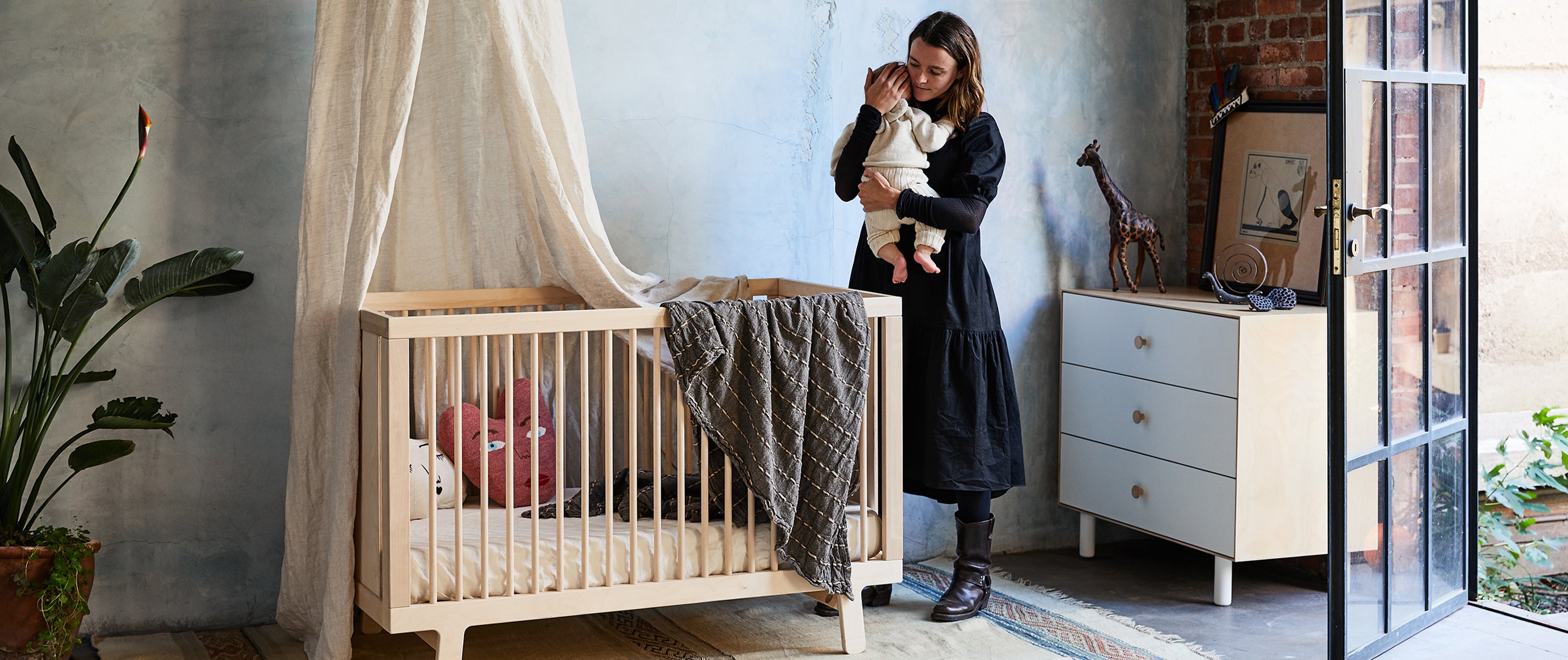 Mom holding baby next to Sparrow crib in nursery