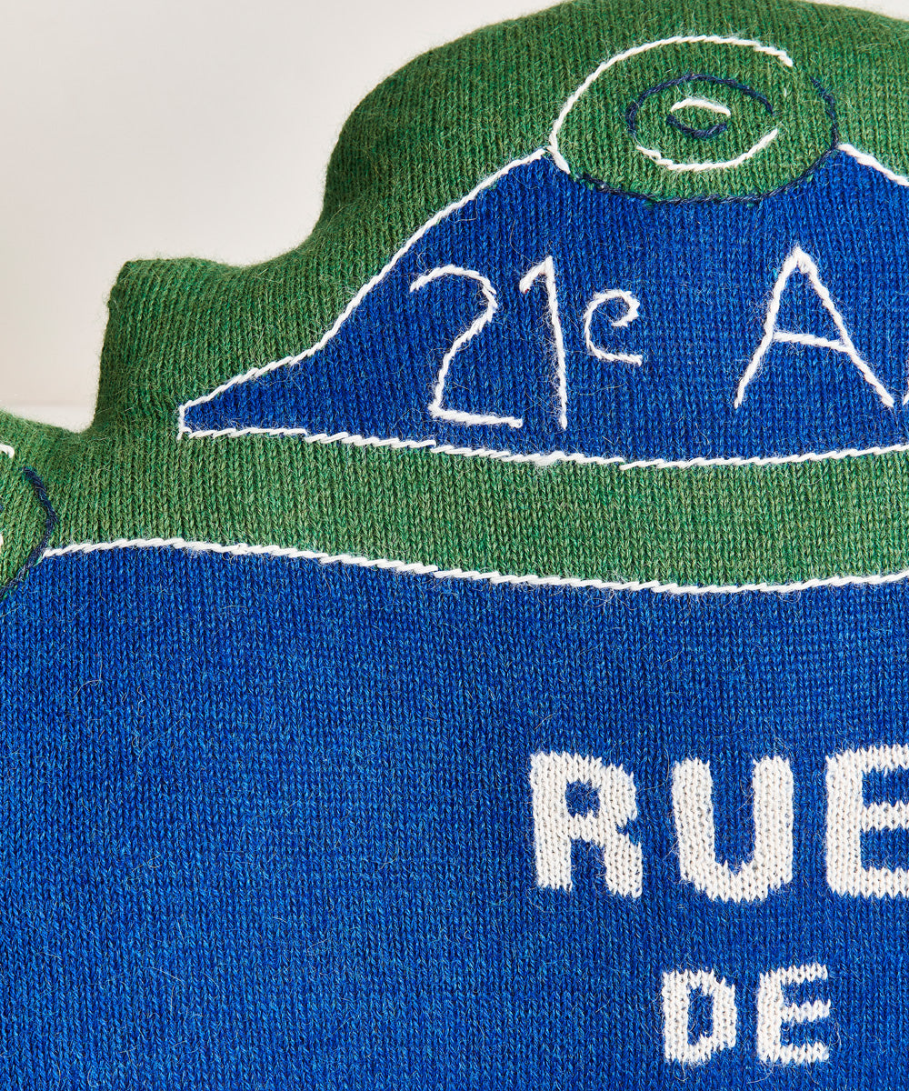 Knitted fabric pillow in blue and green, featuring "21e A" and partial "RUE" text on a white background. Product: Rue de Brooklyn Pillow.