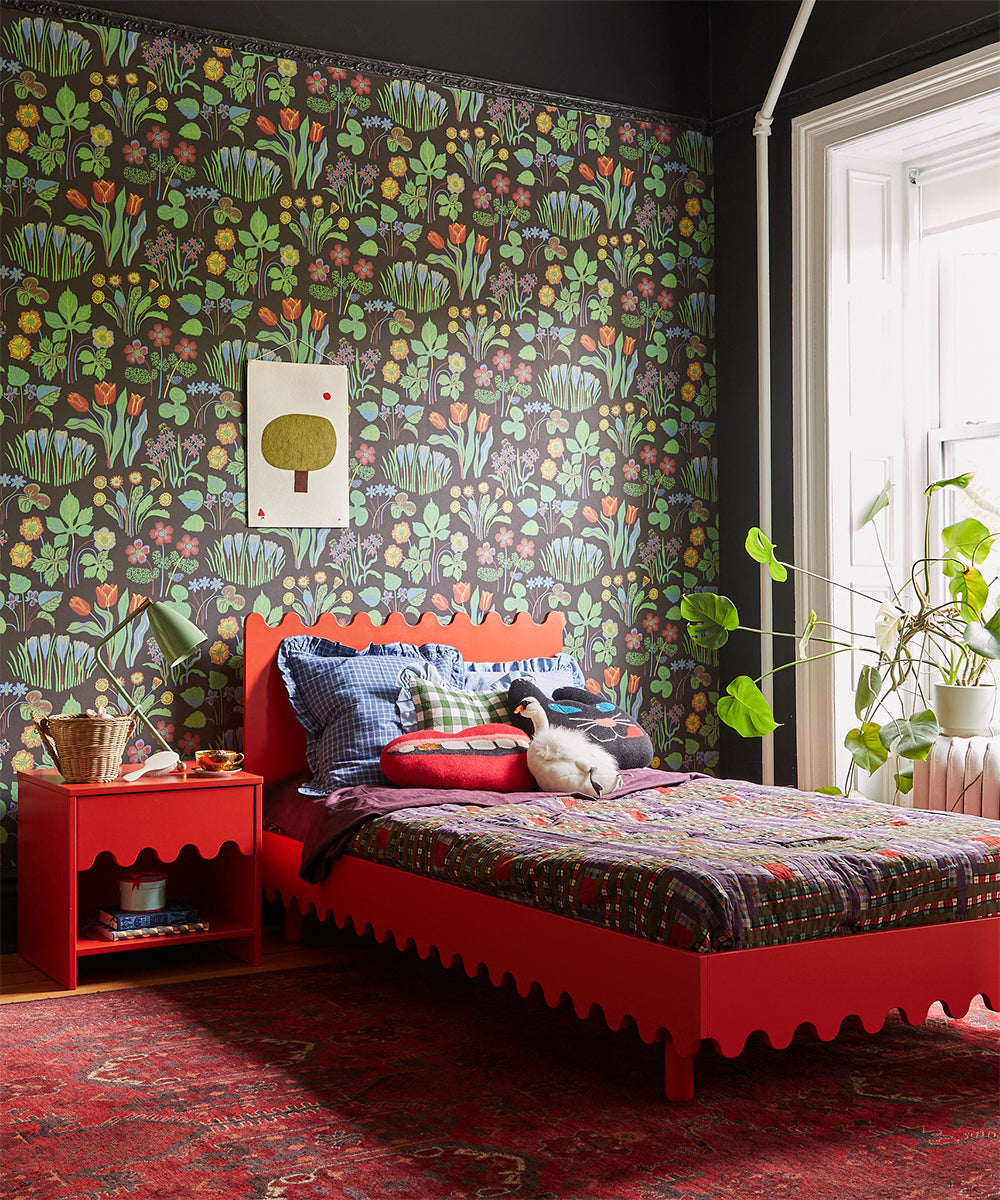 Bedroom with vibrant floral wallpaper, red bed, side table, colorful bedding, and potted plants near a window featuring a Mouth Pillow - Gold Tooth.