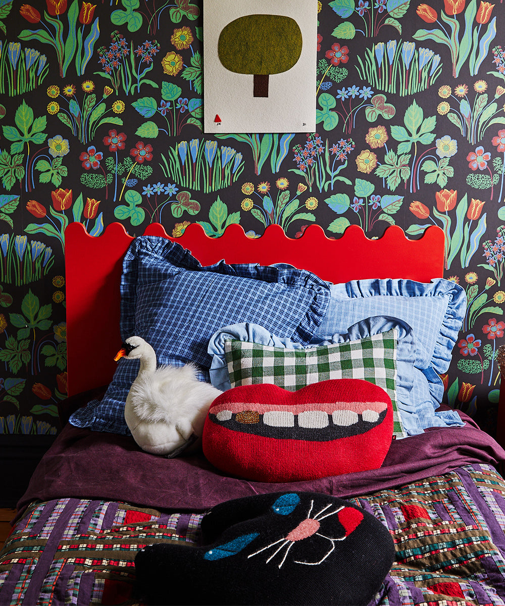 Whimsical bedroom with floral wallpaper, red headboard, and a Mouth Pillow - Gold Tooth among colorful pillows with a duck plush.