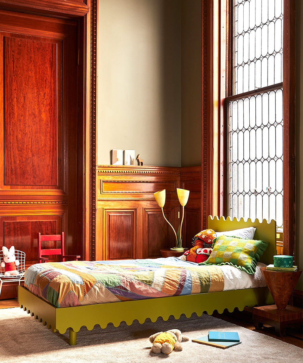 A cozy bedroom featuring the Moss Twin Bed, colorful bedding, stuffed toys, and a large window with wooden paneling.