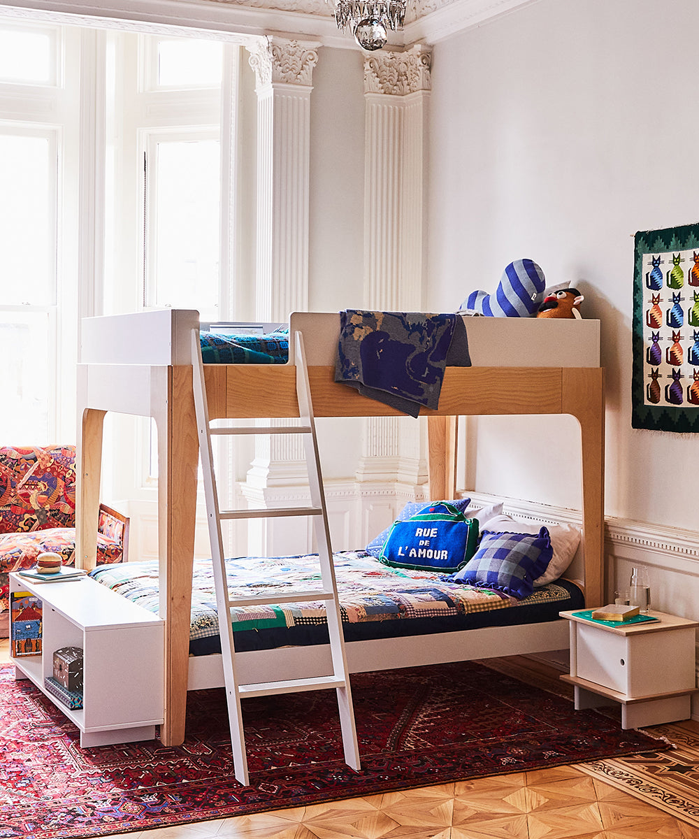 A childrens room features a wooden bunk bed, toys, colorful bedding on a patterned rug near large windows, and the Perch Shelf - Full Size.