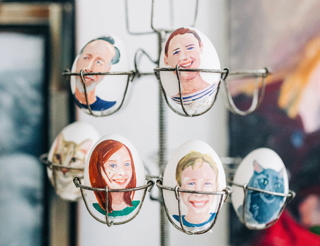 Eggs in a rack, each painted with faces of people and animals.