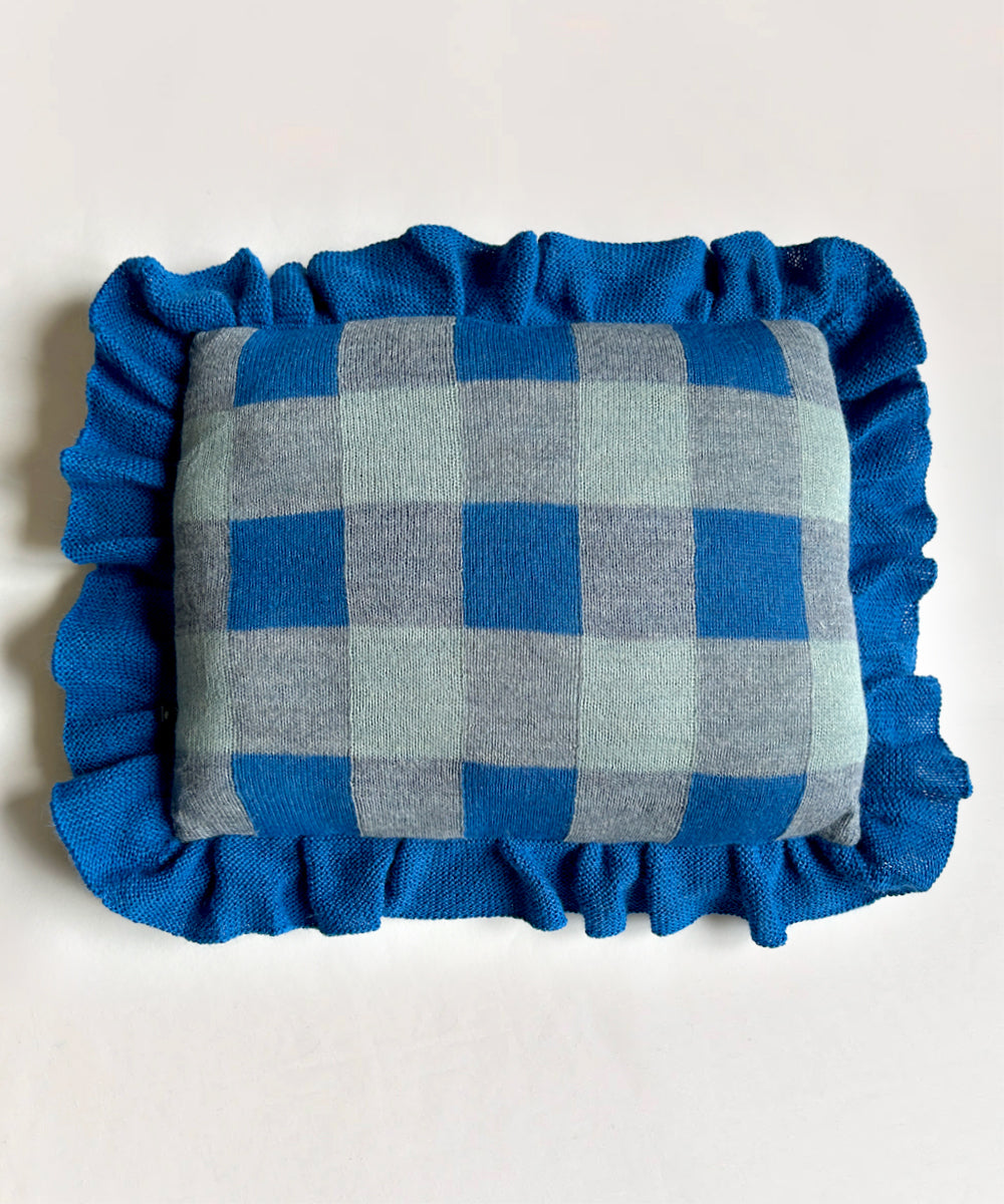 The Gingham Ruffle Pillow has a blue and gray checkered pattern with a ruffled blue edge on a white background.