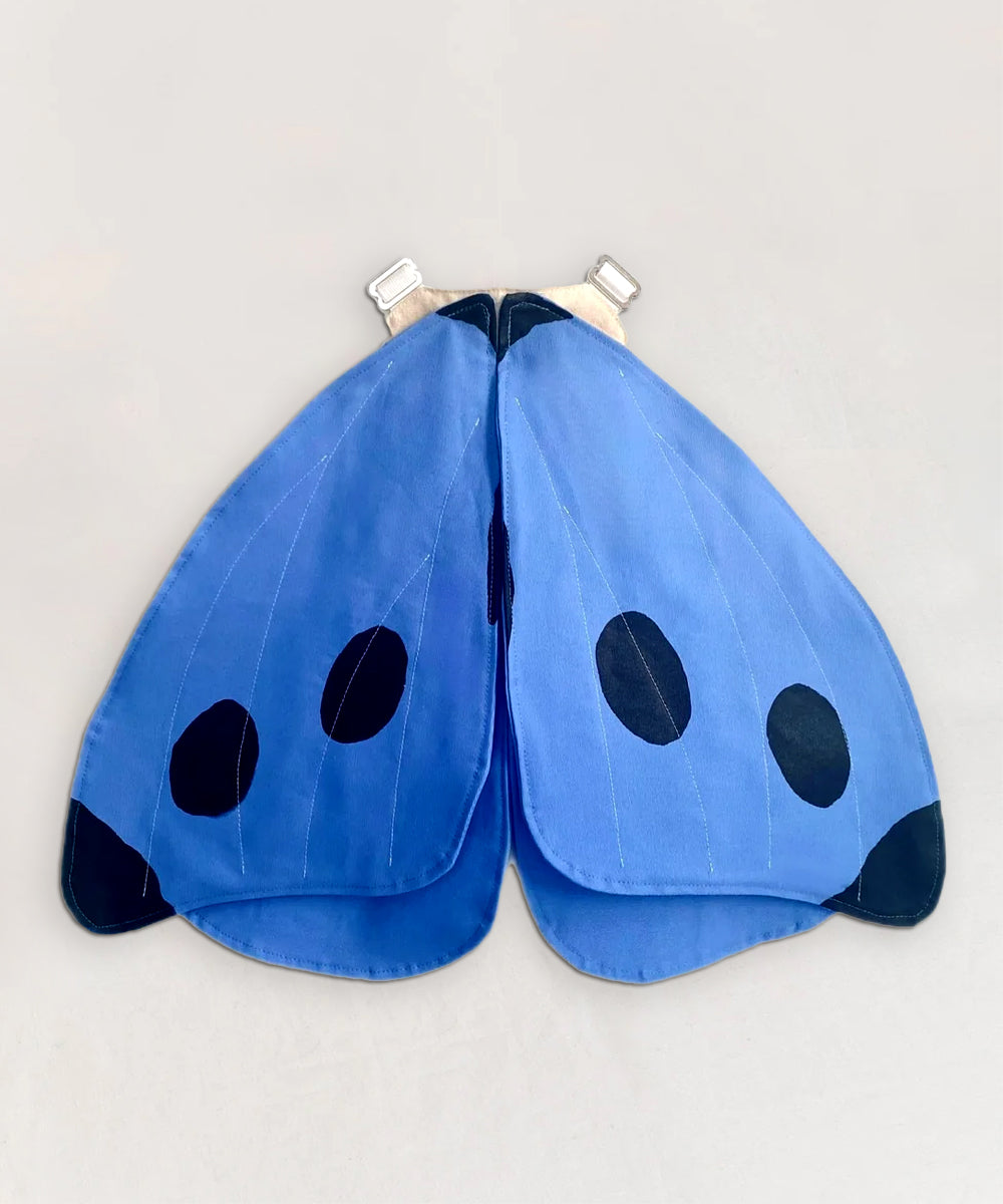 Le Blue Butterfly Wings with black spots on a light gray background.