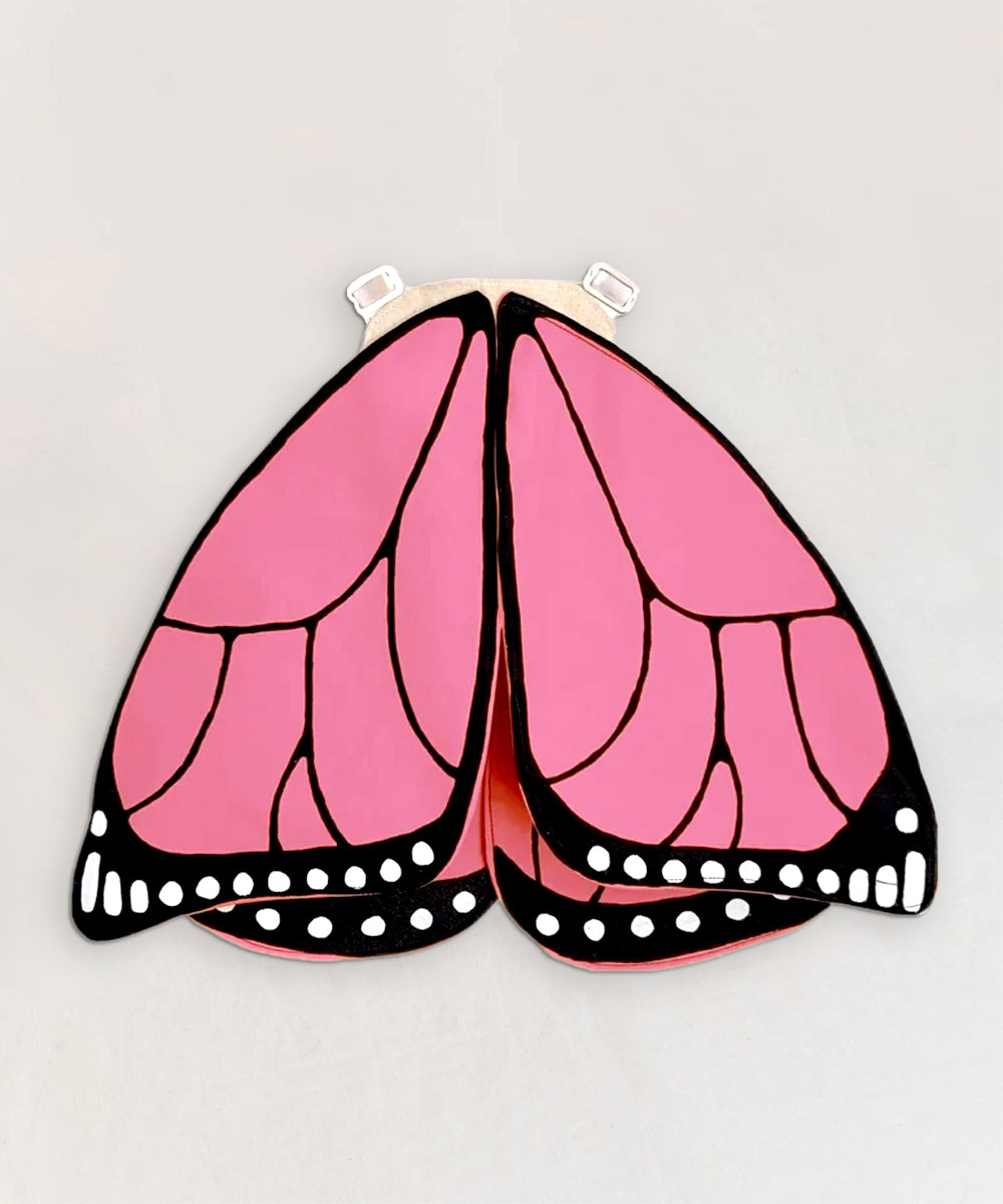 Le Pink Monarch Butterfly Wings feature pink and black wings with white spots, designed as a wearable costume accessory with shoulder straps.