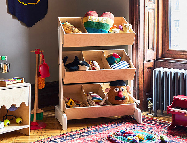 Wooden toy storage organizer with three shelves filled with colorful stuffed animals and toys in a cozy room with a rug and wall decor.