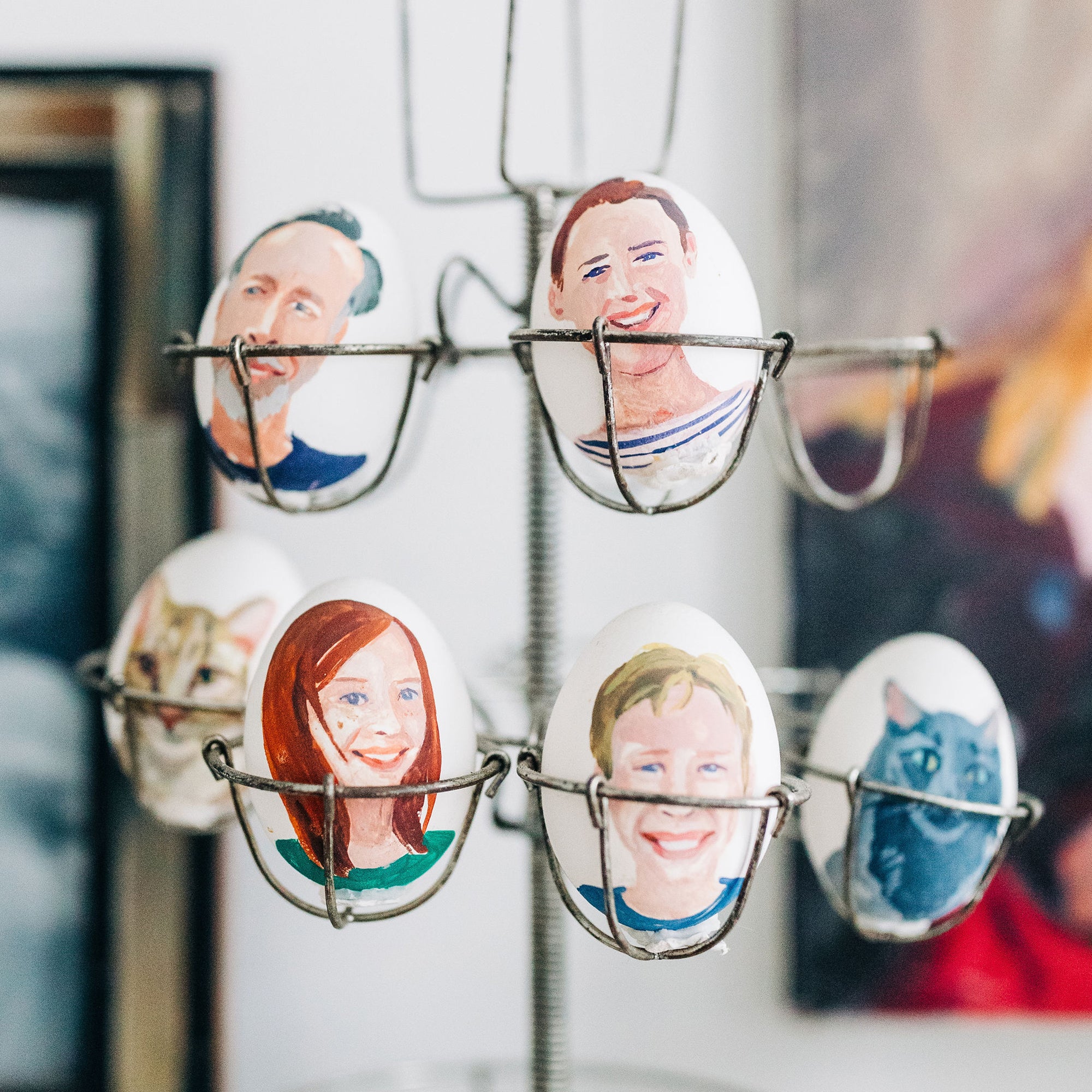 Decorated eggs in a metal holder, each egg painted with a different human face or animal portrait.