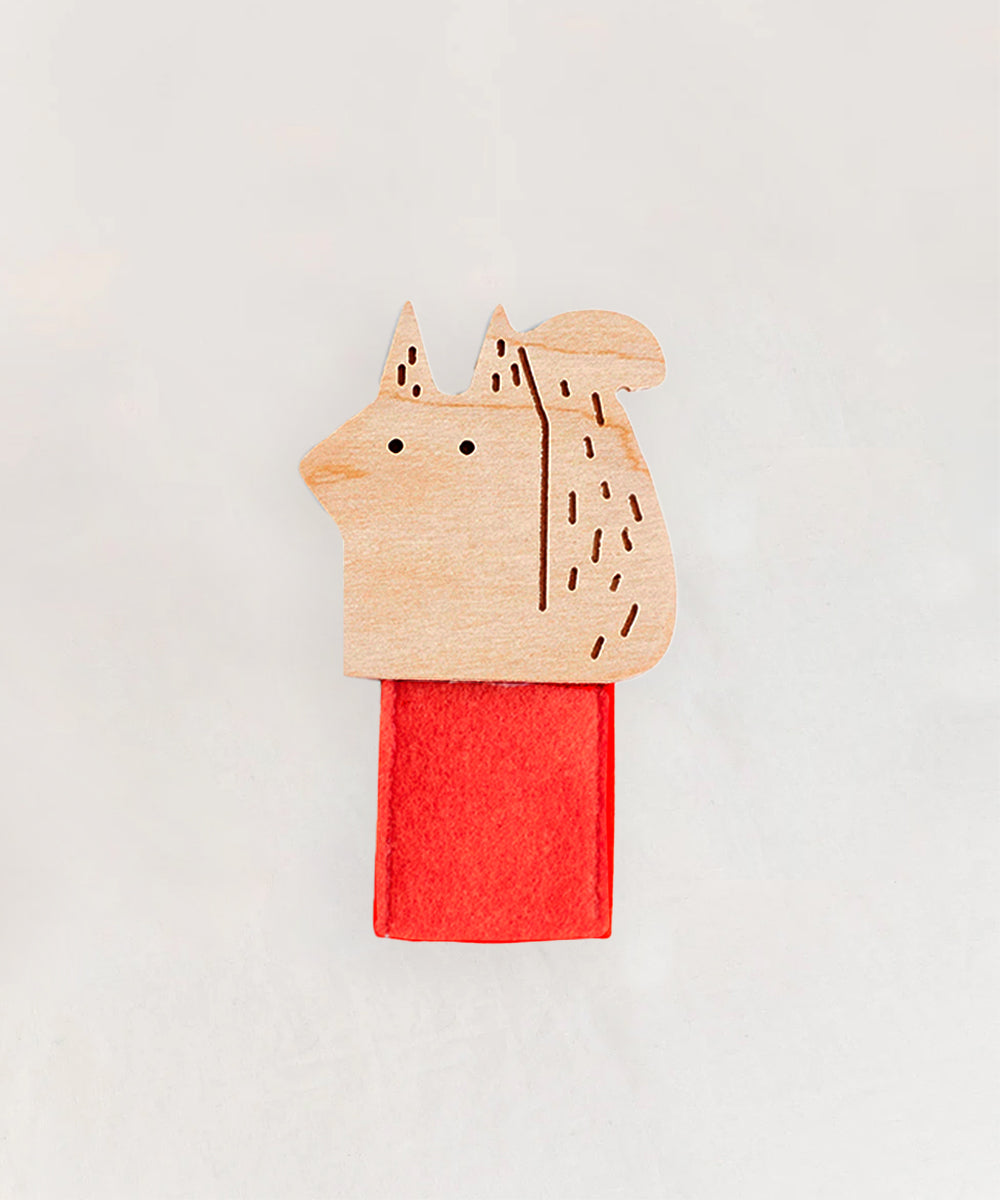 Le Squirrel Finger Puppet is a fox-shaped clip made of wood, featuring engraved details and attached to a red felt strip.