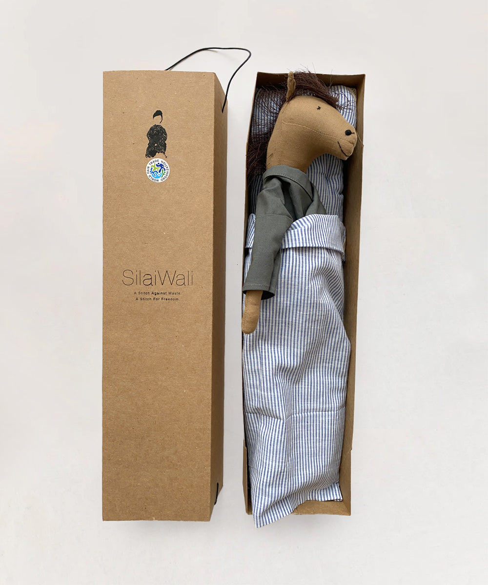 A handmade Le Horsey cloth doll in striped bedding lies next to an open SilaiWali cardboard box.