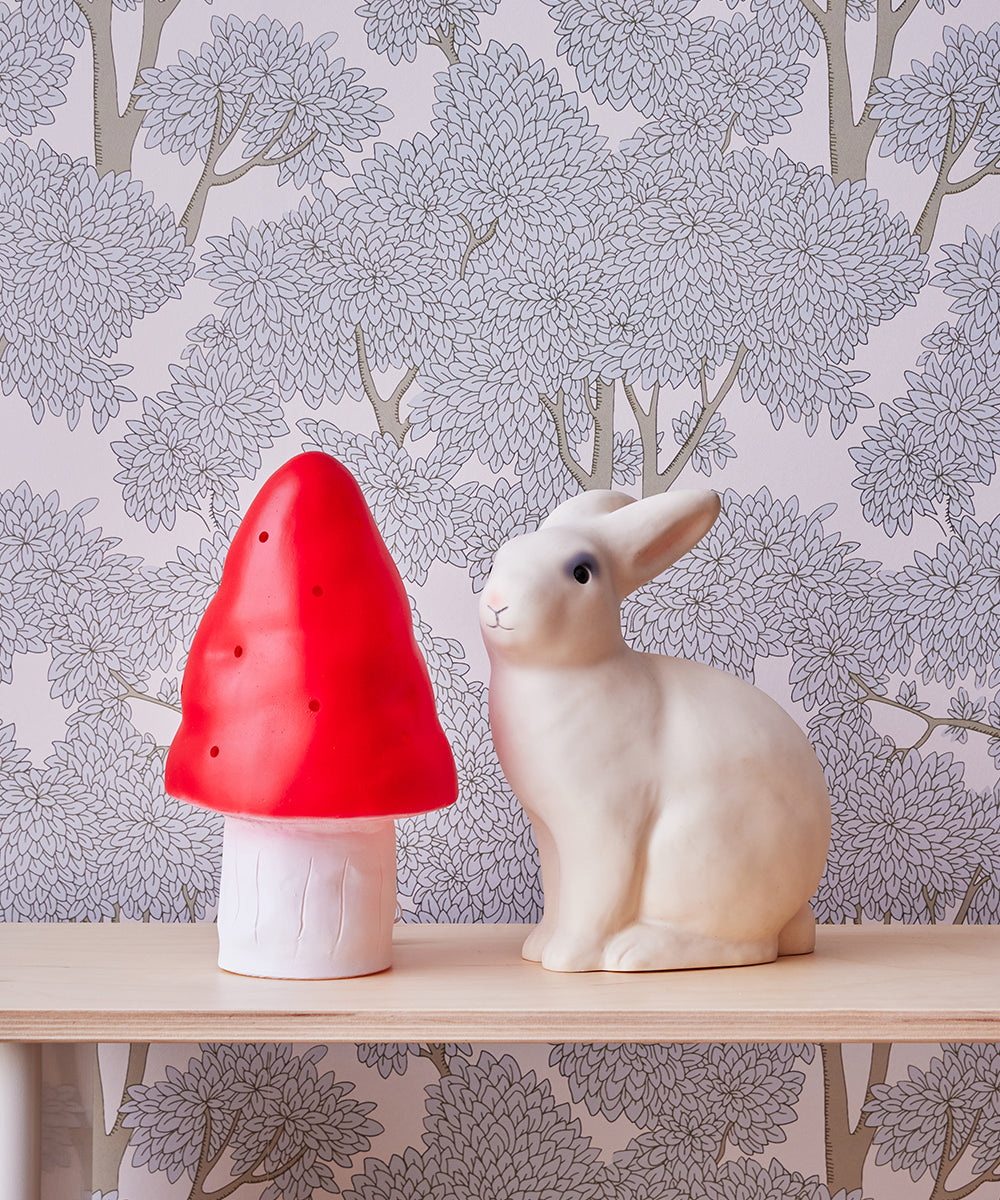 White bunny and Le Small Mushroom Lamp on a shelf against leafy wallpaper.