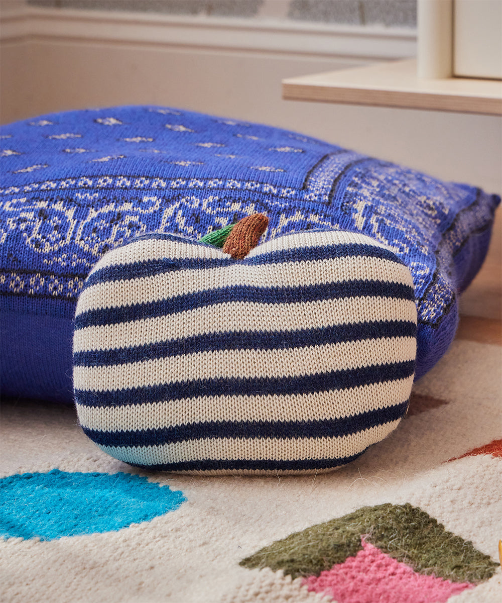 Mini Apple Pillow in front of a large blue cushion on a colorful carpet.