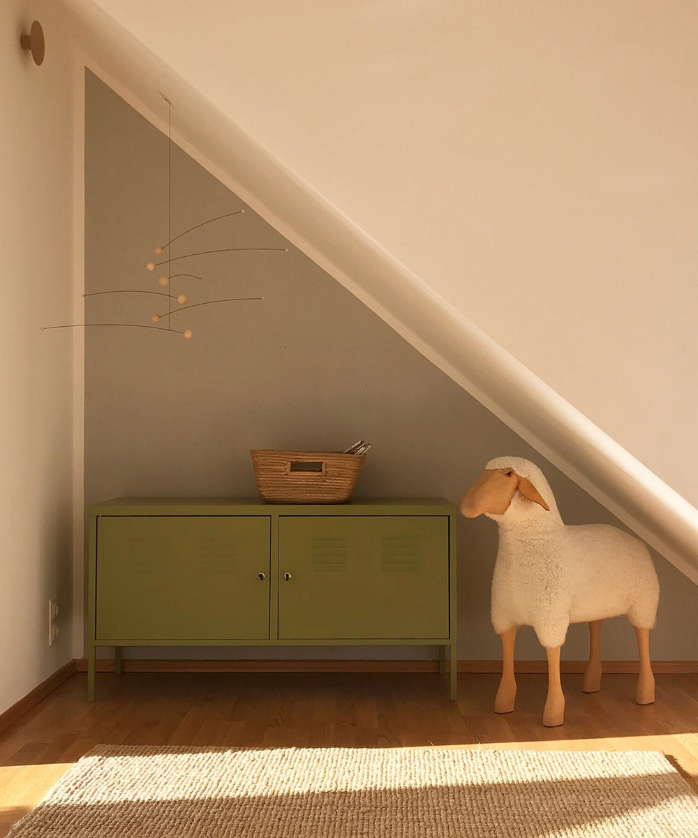 A minimalist room featuring a triangular sloped ceiling, green cabinet, basket, and a large plush sheep on a wooden floor, highlighted by the Le Mobile - Futura Nature.