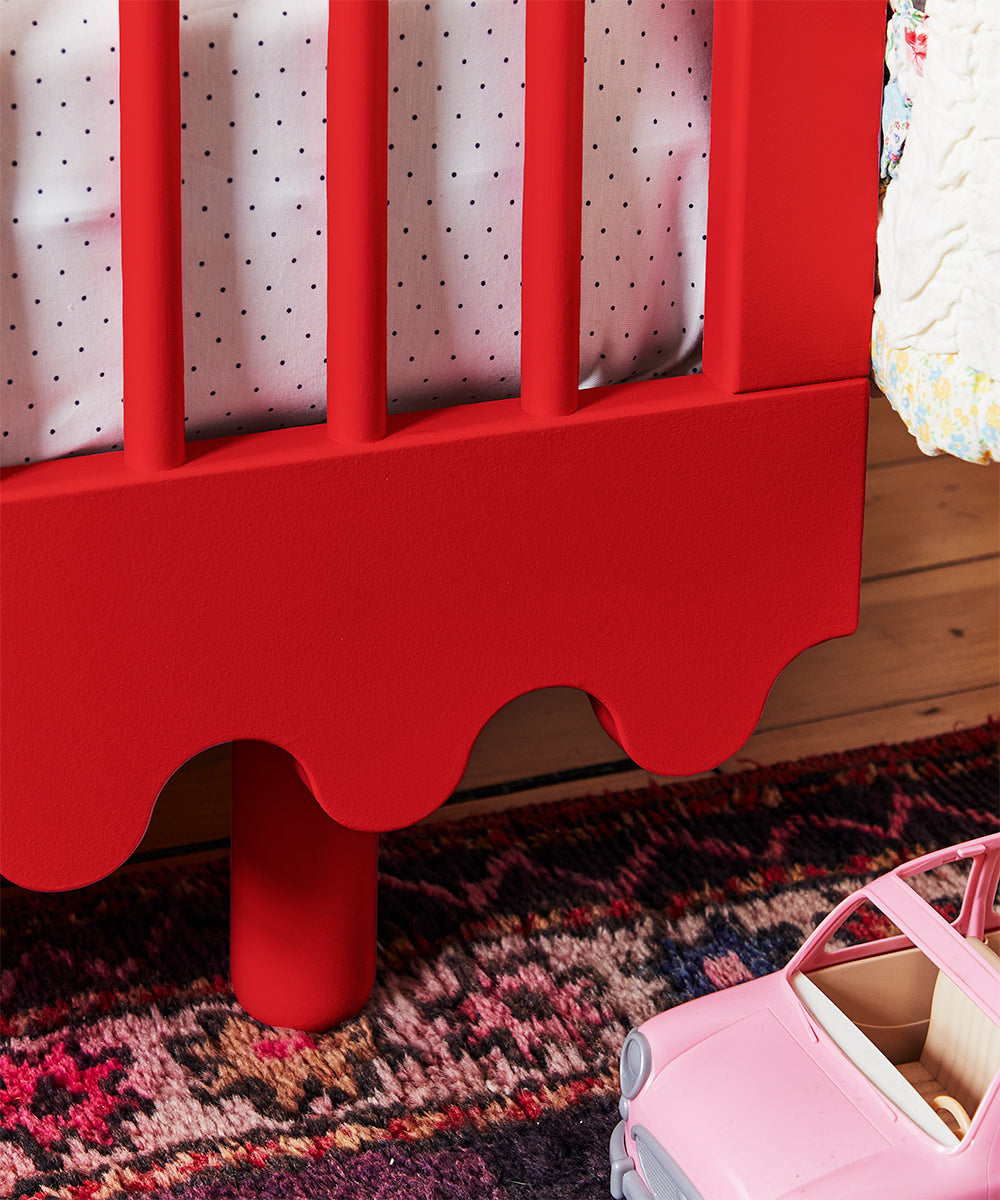 Close-up of a Moss Crib with polka dot bedding, a pink toy car, and a patterned rug on the wooden floor.