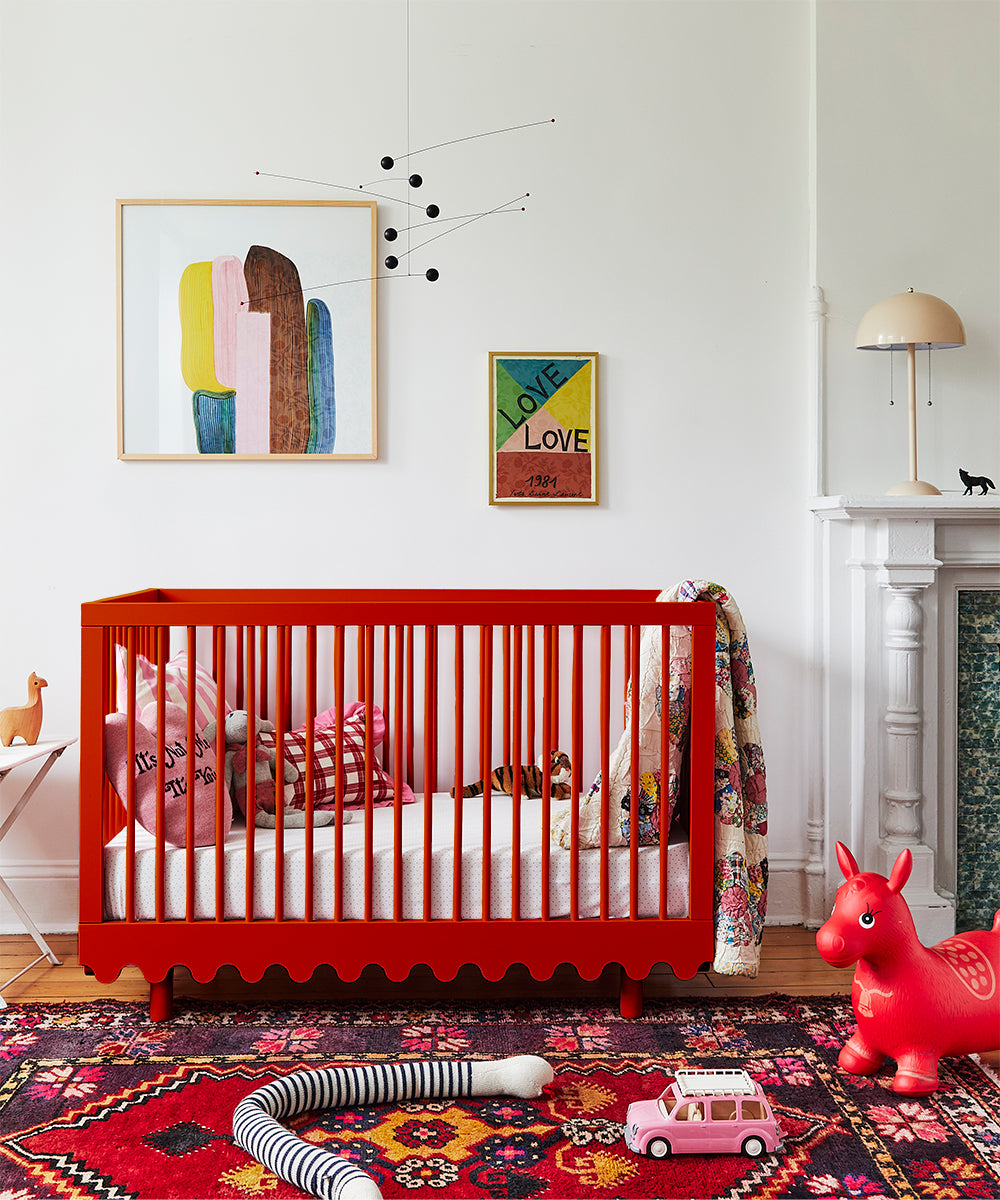 A colorful nursery with a red crib, toys, framed art, a mobile, and the Snake Pillow features bold patterns and bright accents.