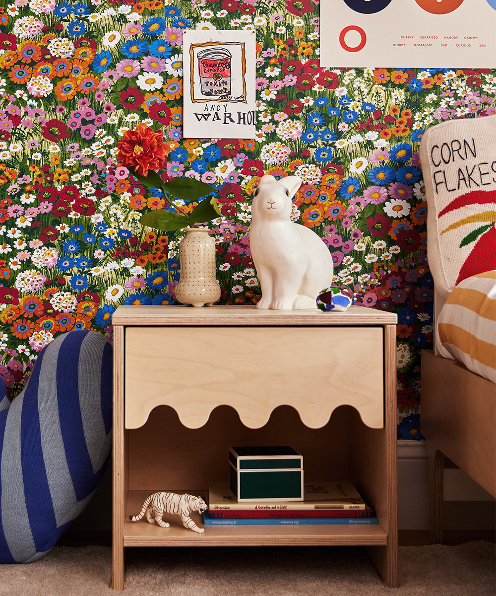 A colorful room featuring floral wallpaper, the Moss Nightstand with scalloped wood detailing, and various decorative items, including a white cat statue.