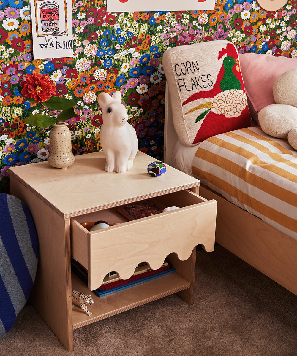 Moss Nightstand with wavy drawer, white rabbit sculpture, floral wallpaper, and a bed with corn flakes pillow.