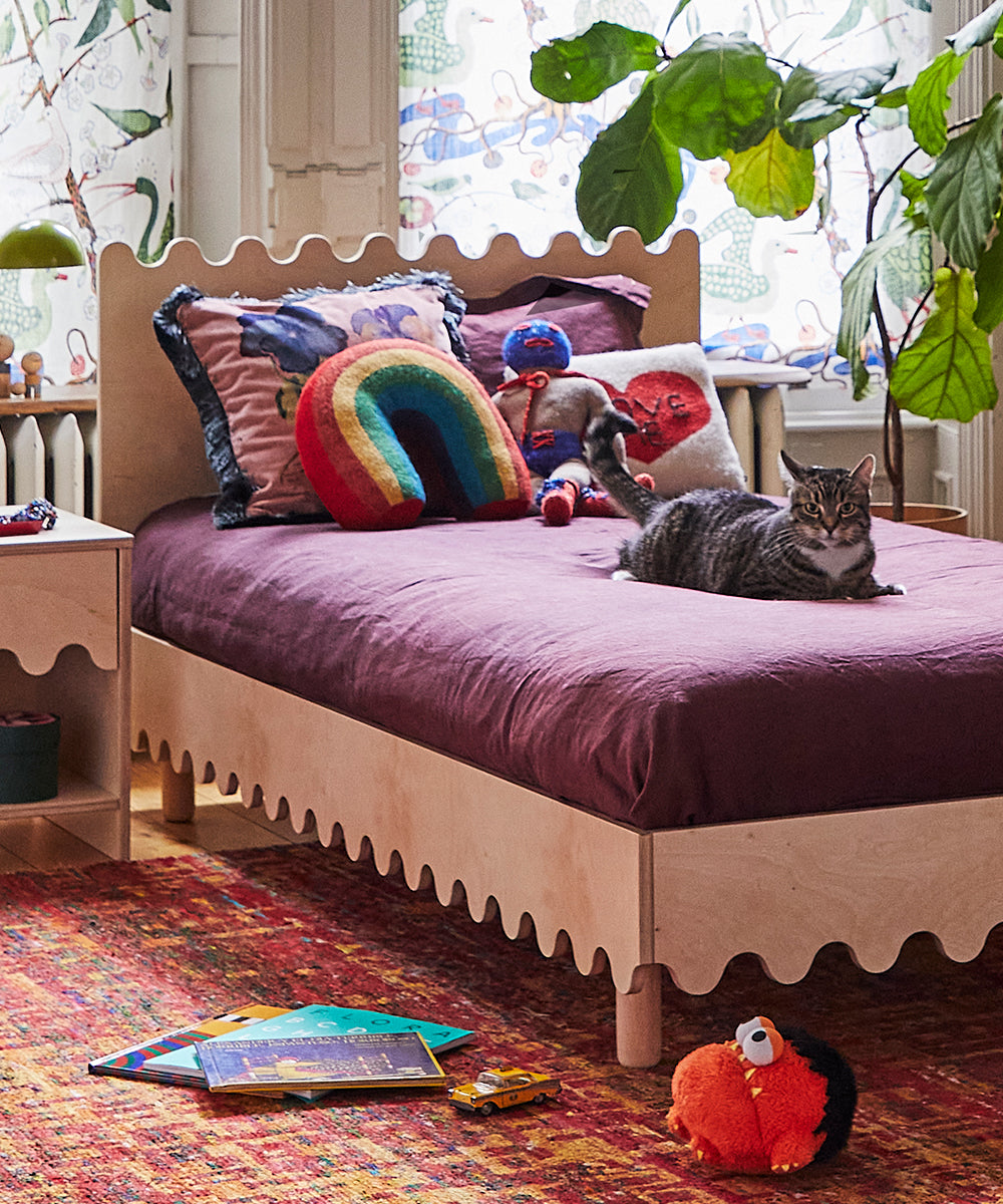 Cozy bedroom featuring a wooden bed, colorful pillows, a cat, a plant, and a Wrestler Doll toy on the floor.