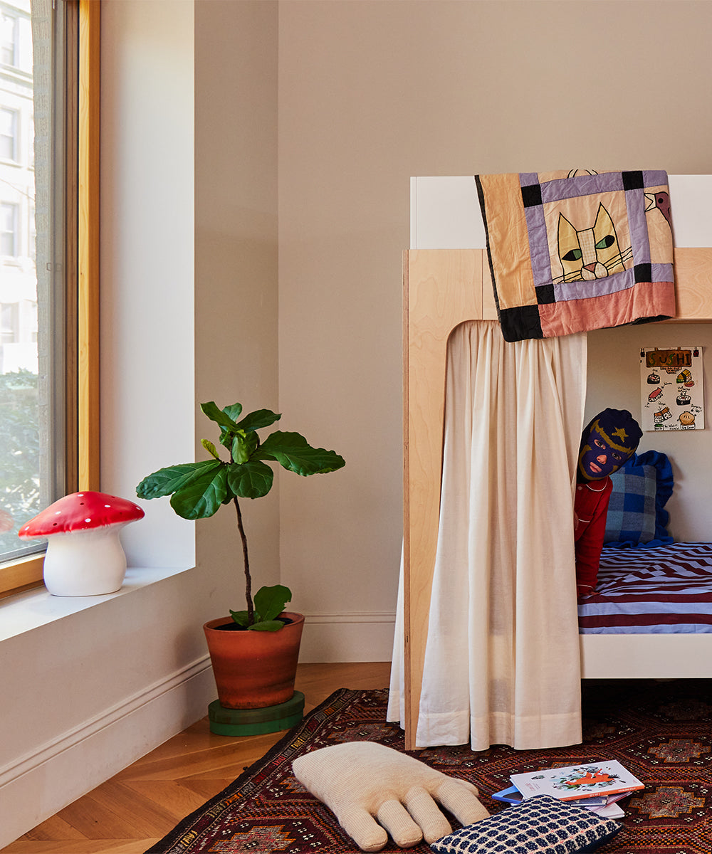 Child wearing a superhero mask in a cozy room on a bunk bed, with the Le Big Mushroom Lamp and a plant nearby.