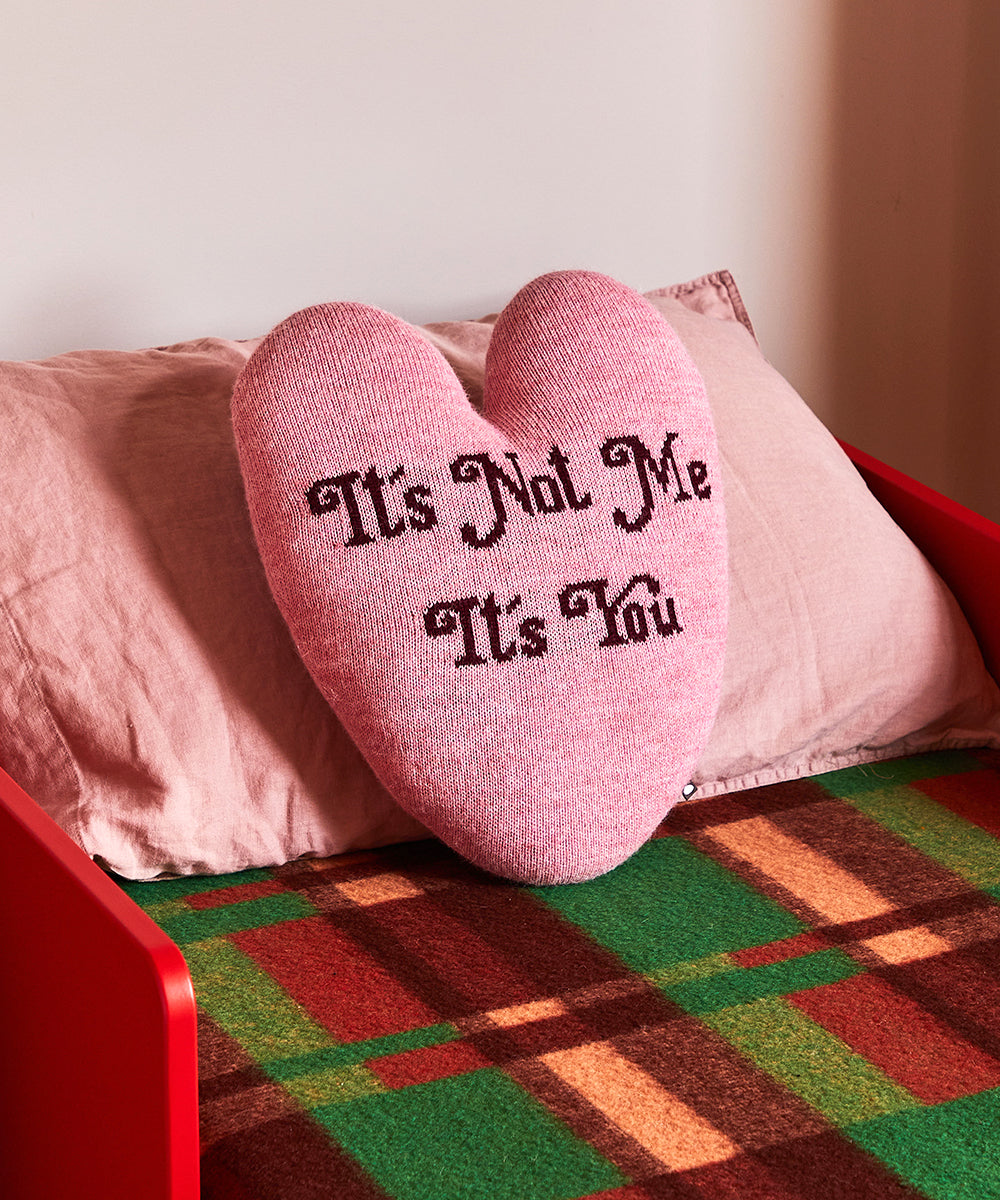 Heart Pillow - It's Not Me, It's You text on a bed with a colorful blanket and red bed frame.