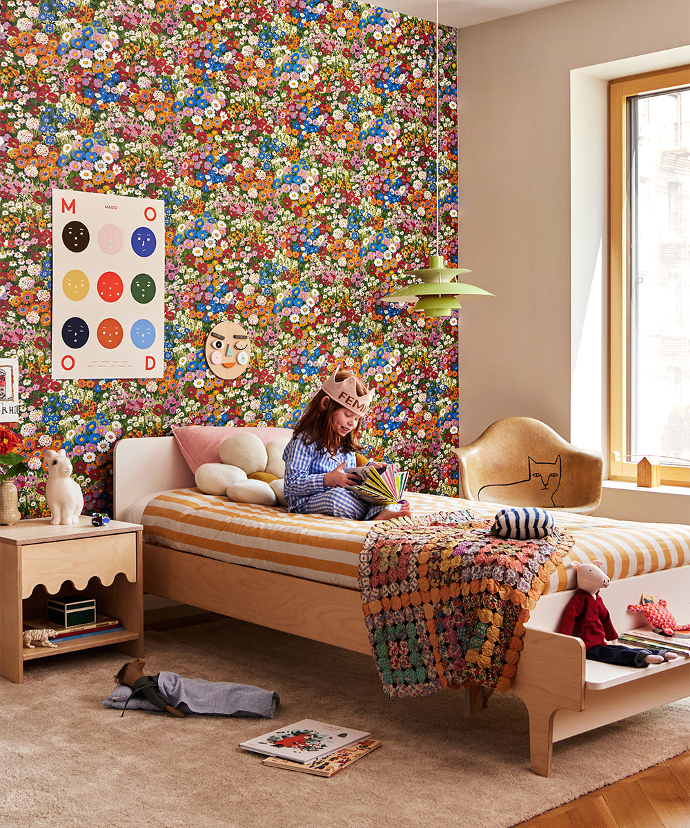 A child reading on a bed in a colorful room with Le Nine Moods Poster, floral wallpaper, art, toys, and vibrant decor.