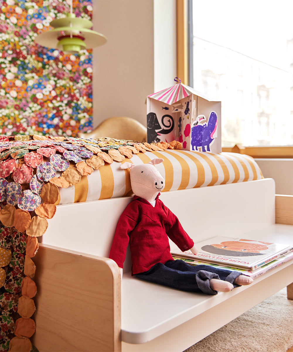 Childs room featuring a colorful quilt on the River Twin Bed, a stuffed animal on the bed, a bookshelf filled with books, and a toy house situated near the window.