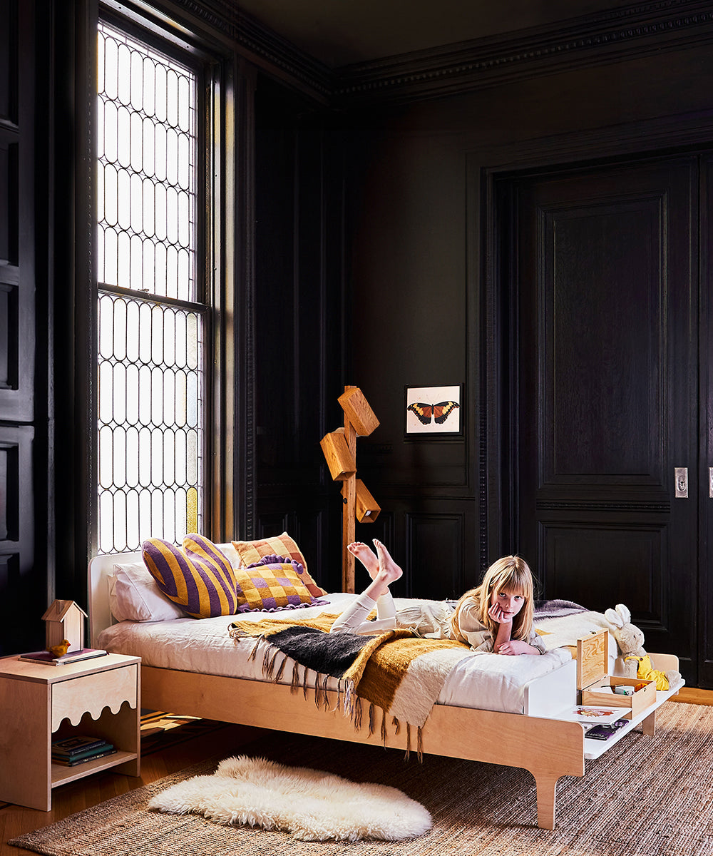 Child resting on a Dual Firm Twin & Full-Size Mattress in a chic, dark-walled room with a large window and wooden decor accents.