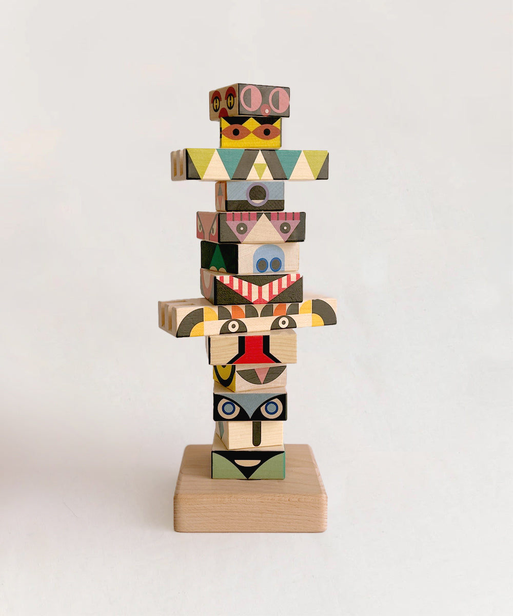 The Le Totem Stacker consists of wooden blocks featuring colorful, abstract patterns and face-like designs set against a plain background.