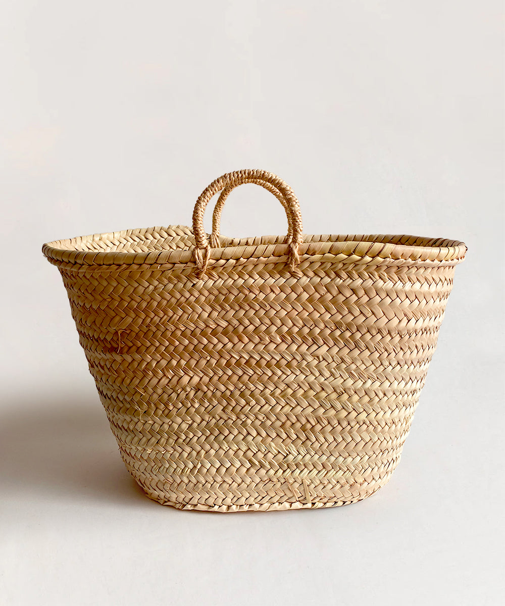 A large woven straw basket called Le Market Basket, featuring two small handles, set against a neutral background.