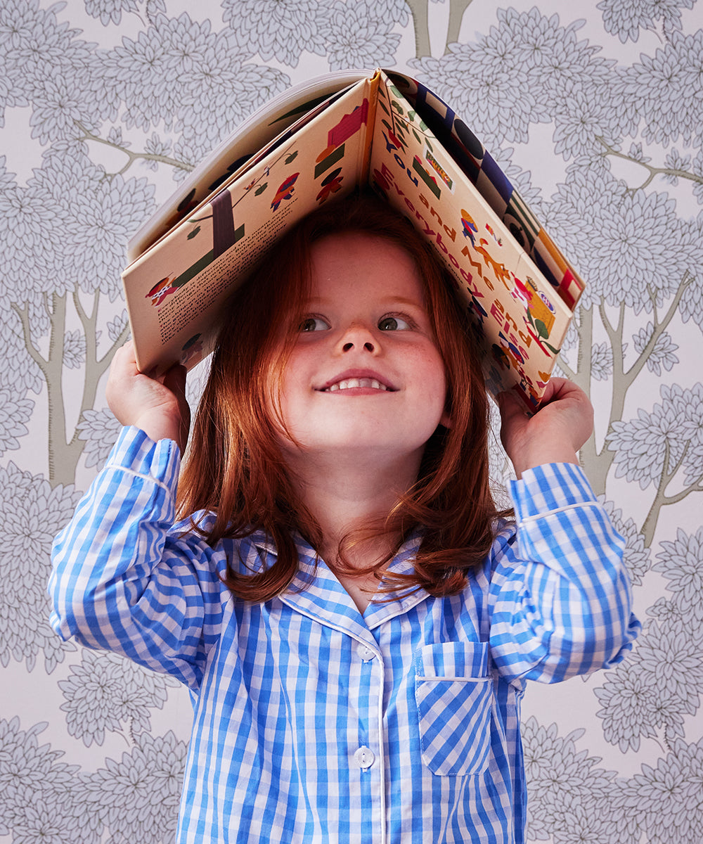 A child with red hair in a blue checkered shirt holds Le Book - You and Me and Everybody Else open above their head.