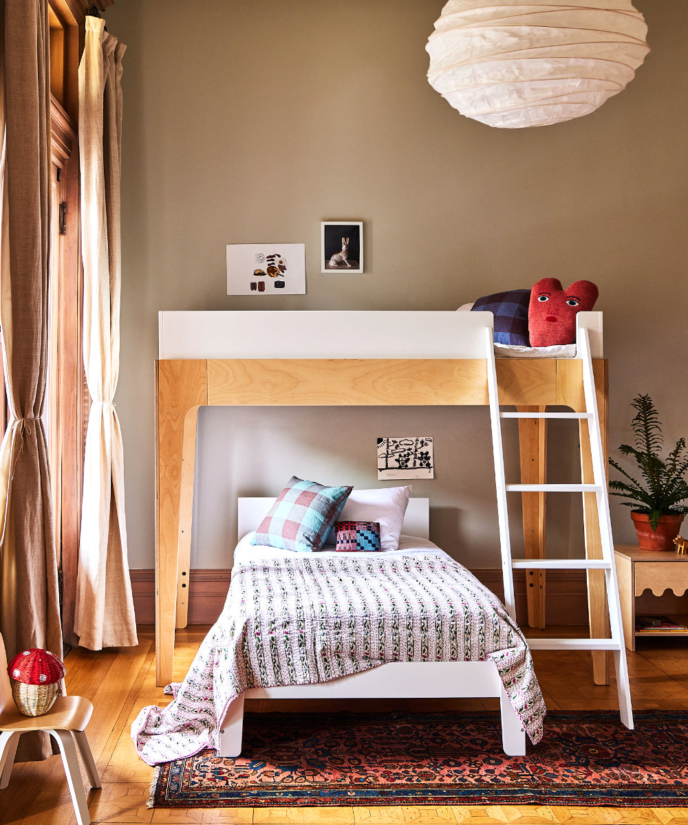 Cozy bedroom featuring a Perch Twin Bunk Bed with ladder, twin bedding, colorful accents, wall art, and an indoor plant on wooden flooring.