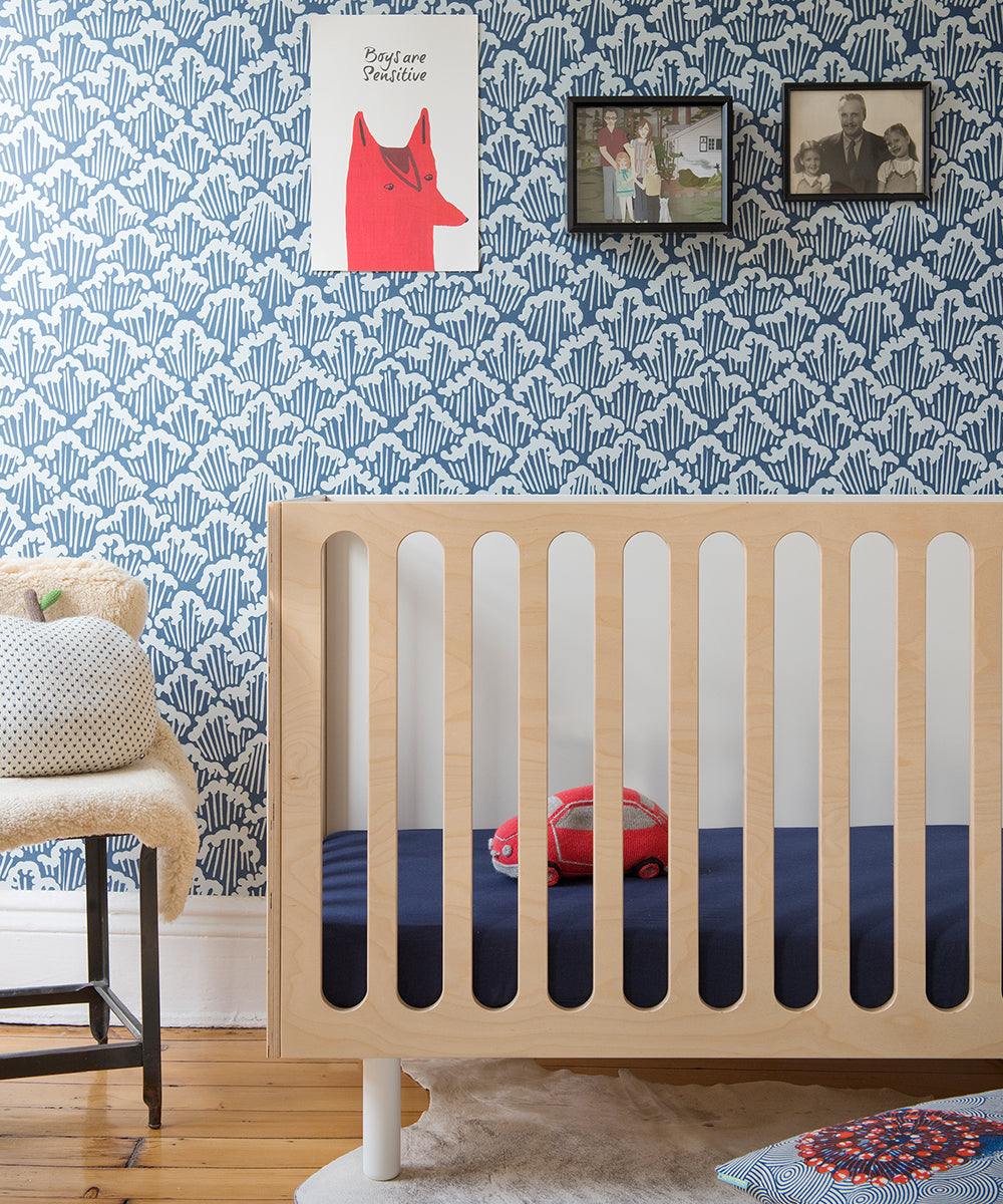 Nursery featuring the Fawn 2-in-1 Crib System, blue patterned wallpaper, and wall art. A red toy car sits on a navy sheet.