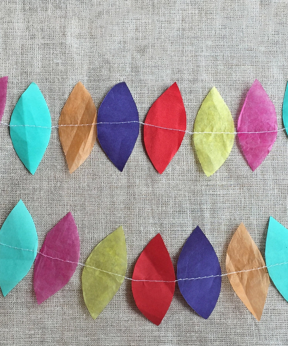 The Le Teardrop Garland features colorful paper leaf shapes sewn in two horizontal rows, creating a decorative touch against a beige fabric backdrop.