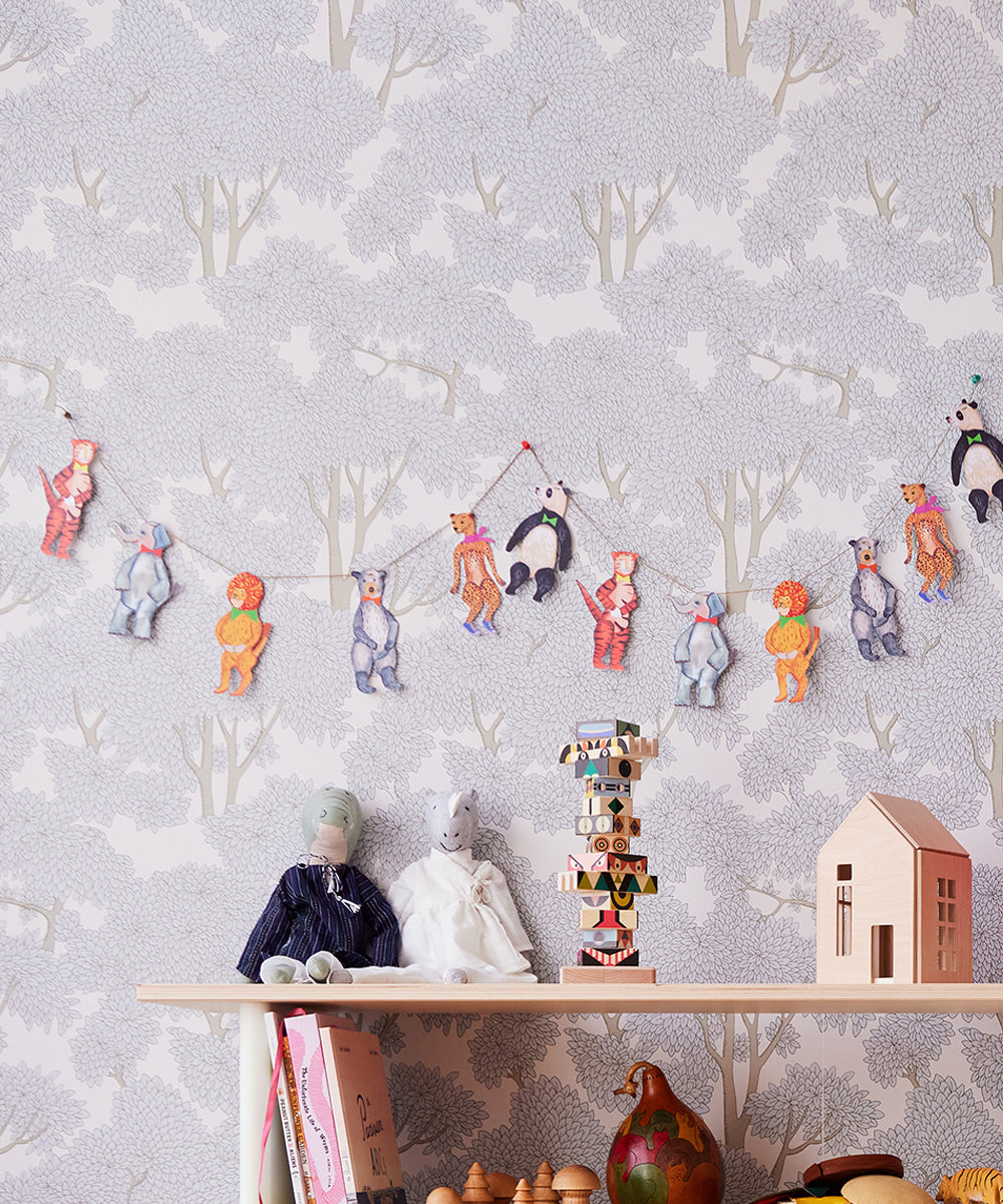 A childs room decorated with animal-themed wallpaper features a shelf filled with books, toys, and dolls. A Le Garland - Animal Parade of animal cutouts hangs above, adorning the wall.