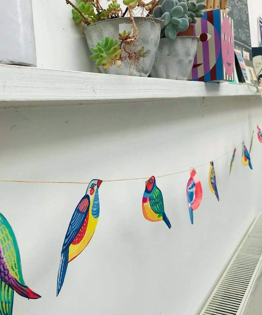 Le Garland - Colorful Birds are displayed along the wall under a shelf with potted succulents.