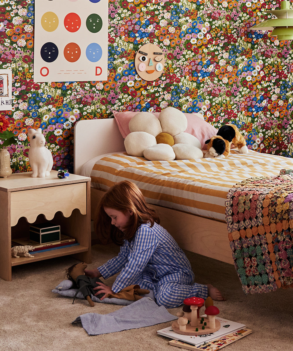 Child sitting on a carpet in a colorful bedroom, playing with Le Horsey toys surrounded by floral wallpaper and striped bedding.