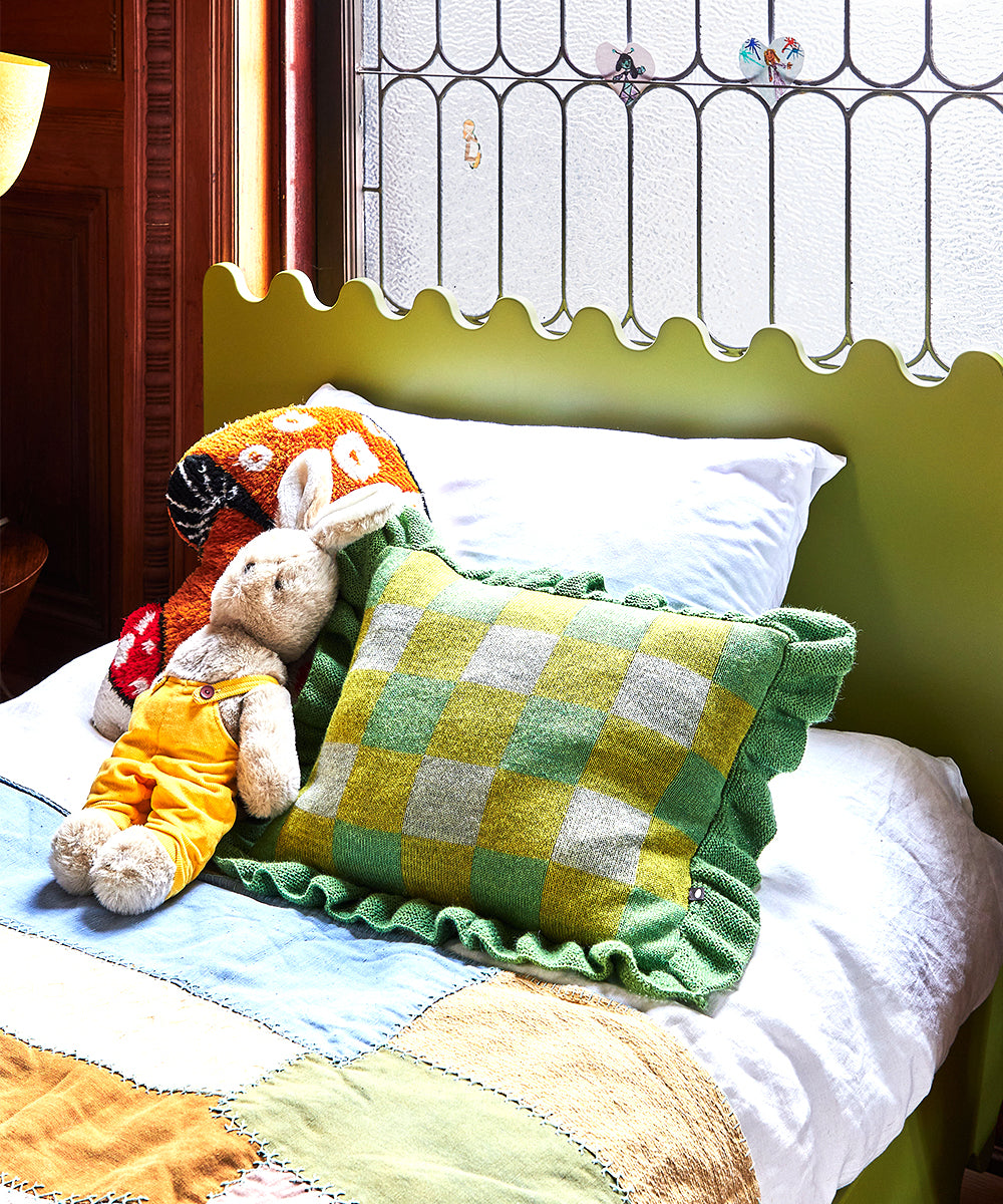 The Moss Twin Bed features a decorative headboard, adorned with stuffed animals and a green checkered pillow, set by a window for a cozy childrens bedroom.