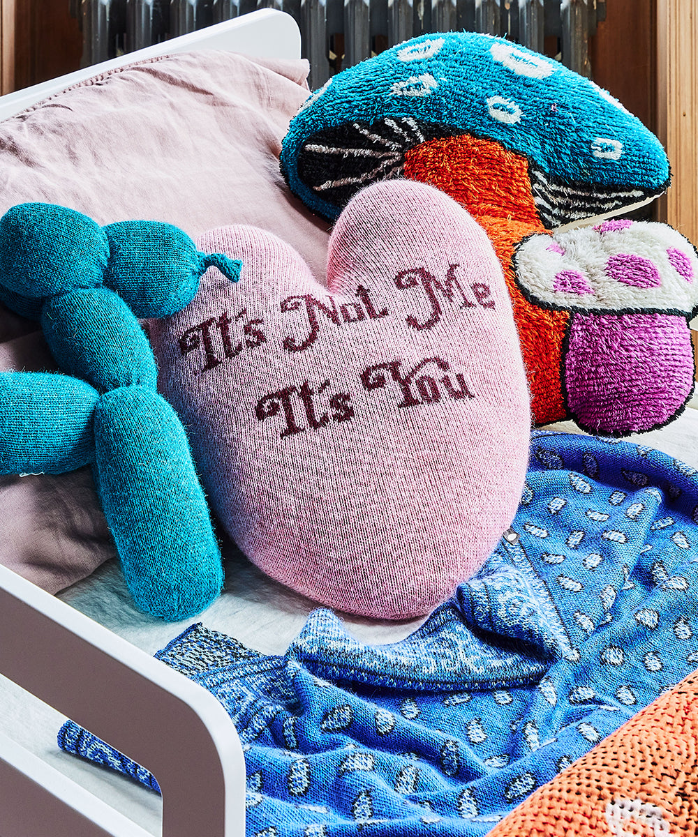 A cozy bed featuring a Heart Pillow - It's Not Me, It's You, alongside blue dog and colorful mushroom pillows.