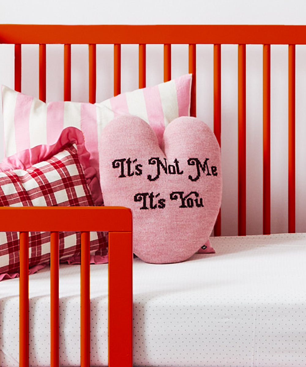 Heart Pillow - It's Not Me, It's You on a red crib, surrounded by red and pink striped pillows.