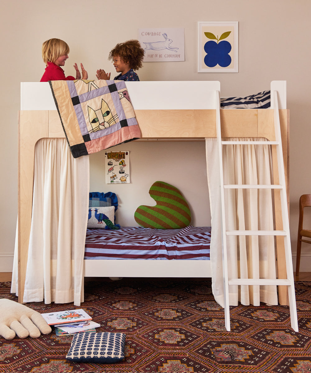 Children enjoying the Perch Twin Bunk Bed with quilts and cushions in a cozy, decorated bedroom.