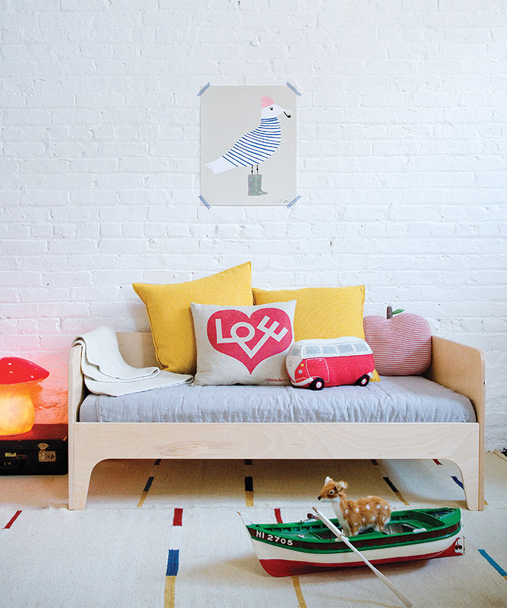 A childrens room features the Perch Toddler Bed, vibrant cushions, a toy boat, and a poster mounted on a white brick wall.