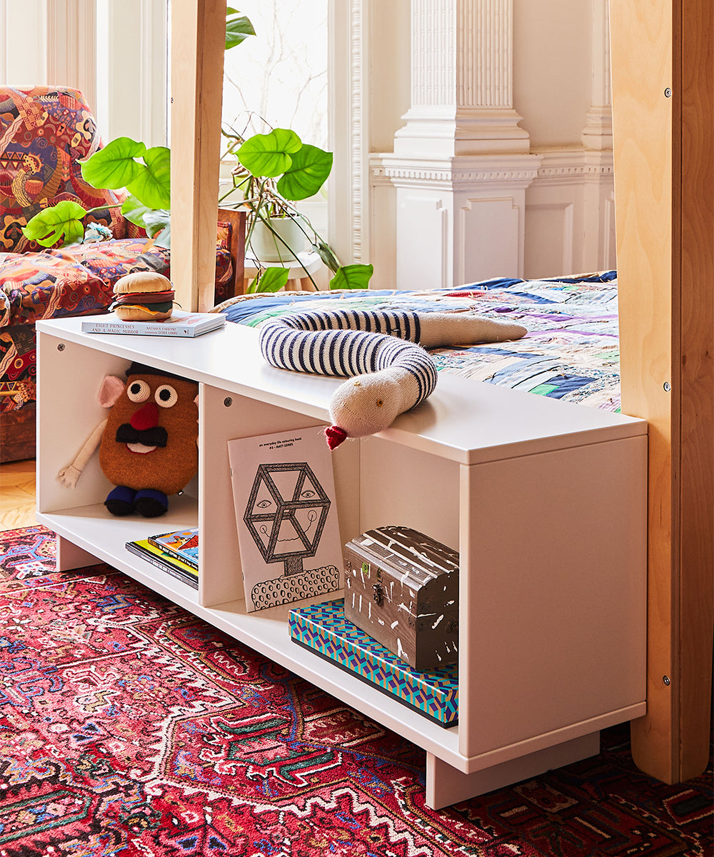 Children's room with a white shelf, toys, books, a striped toy snake, a colorful rug, and a Funny Face Pillow in a cozy setting.