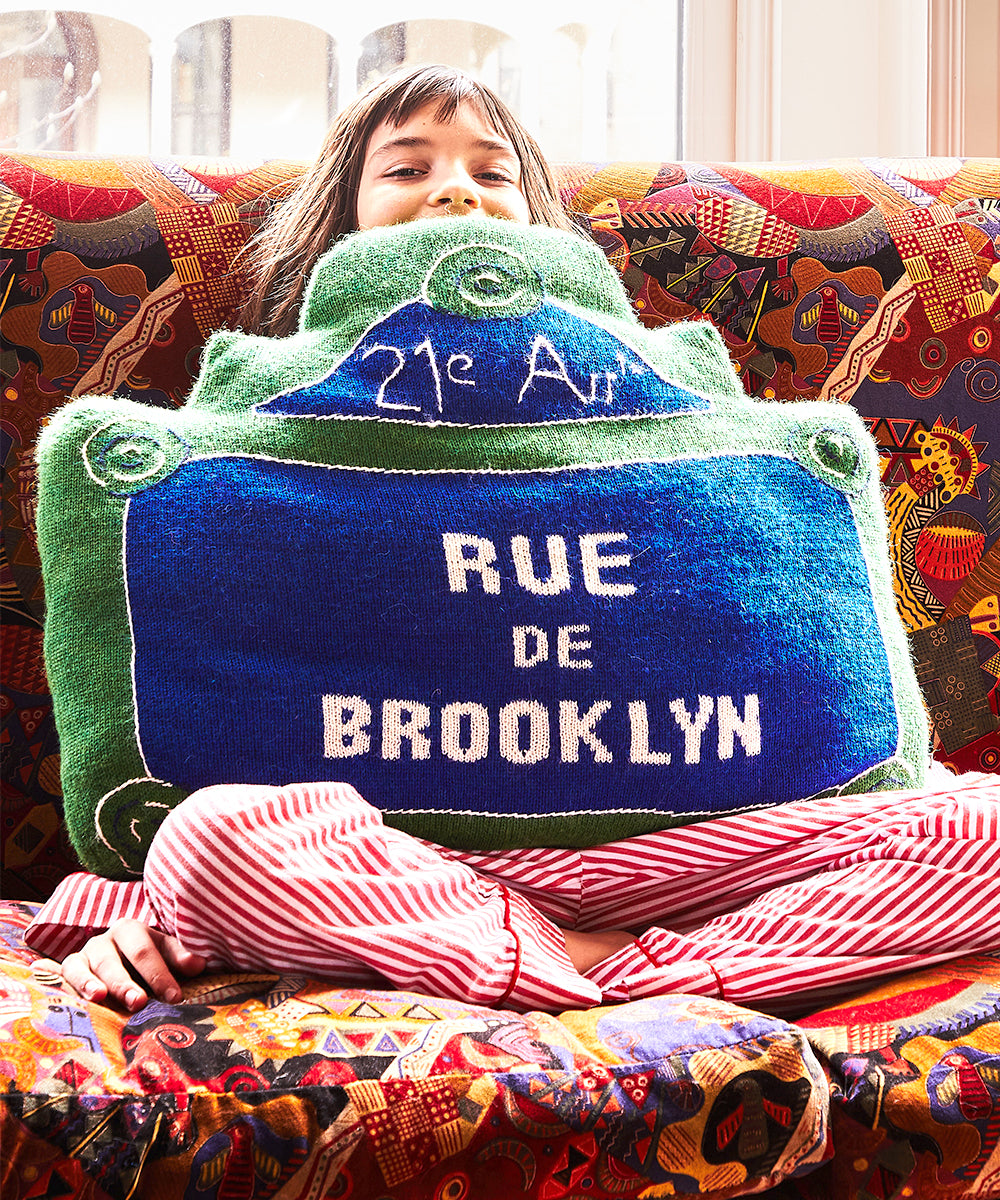 Child on a patterned couch with a Rue de Brooklyn Pillow, wearing striped pants.