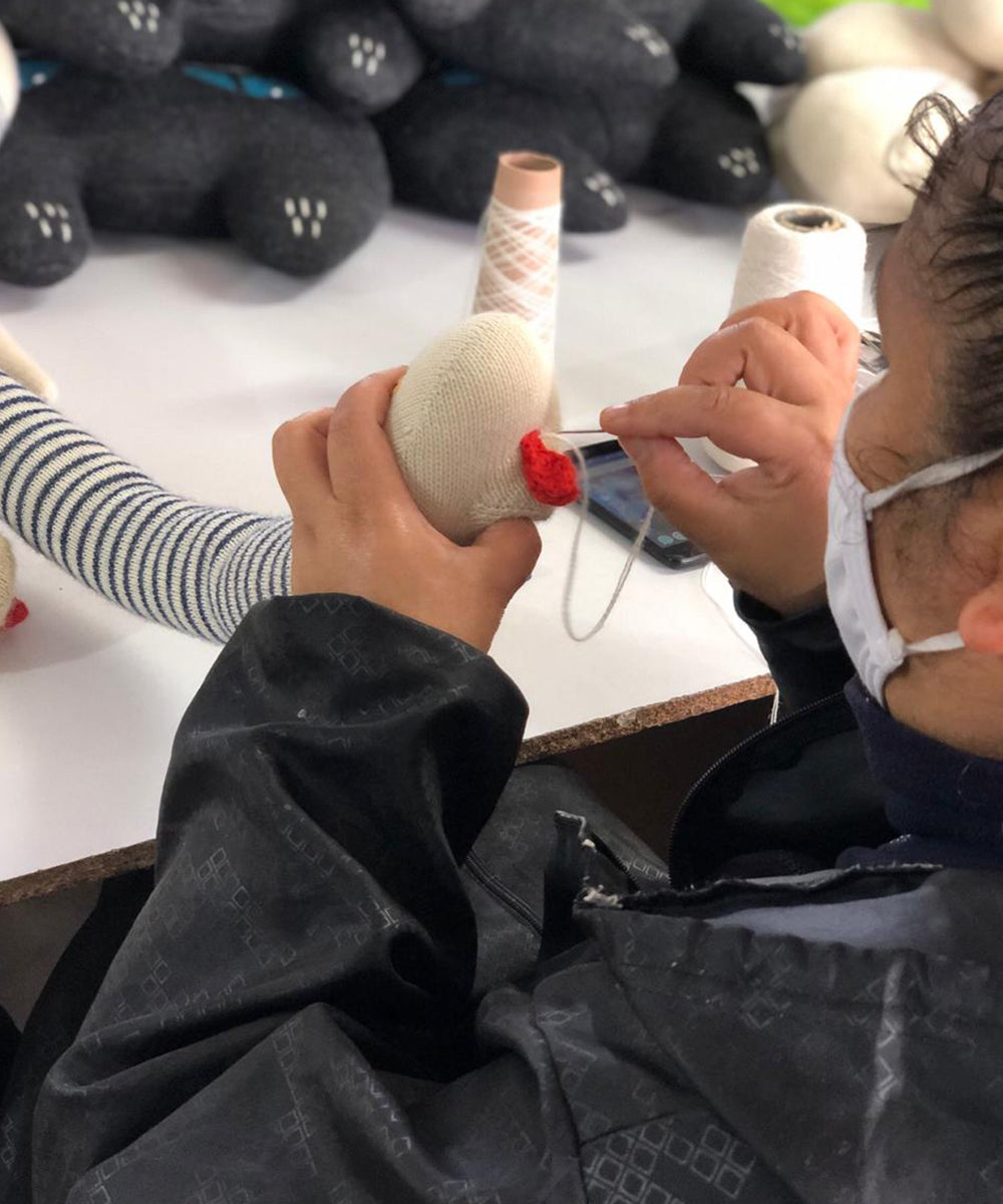 Person sewing a red detail onto a Snake Pillow with black and white thread spools nearby.