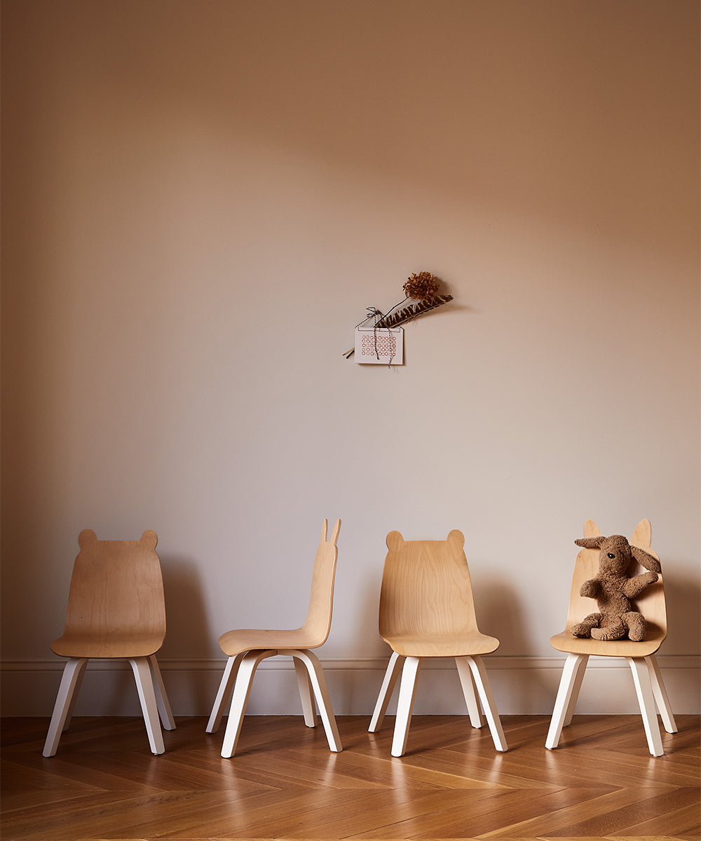 Two sets of Bunny Play Chairs, each featuring a unique backrest design, line a wall with a brown teddy bear on one chair.