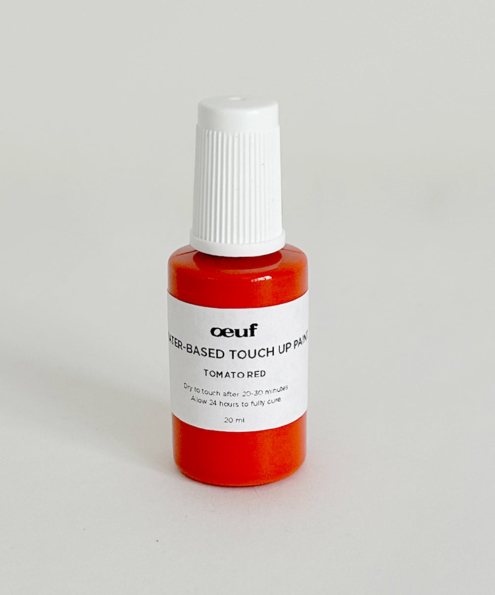 A small, red bottle labeled Touch-up Paint: Tomato Red sits on a light surface.