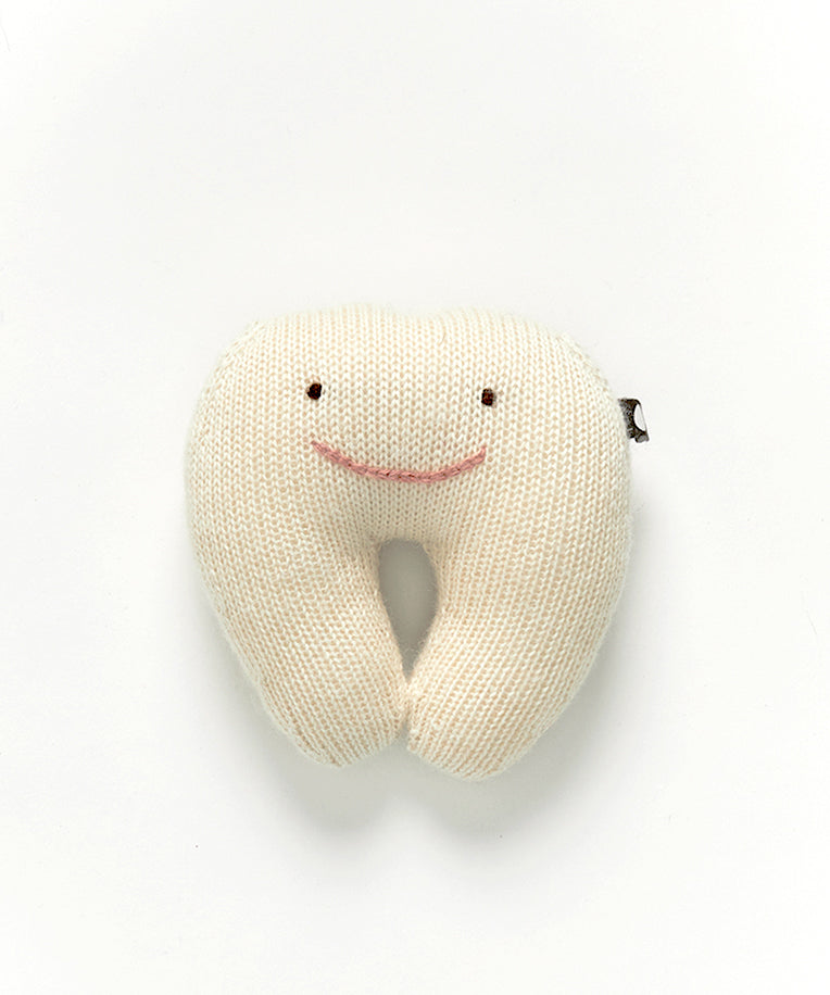 A "Tooth Fairy Pillow" is a knitted plush toy shaped like a tooth, featuring a smiling face on its white surface.