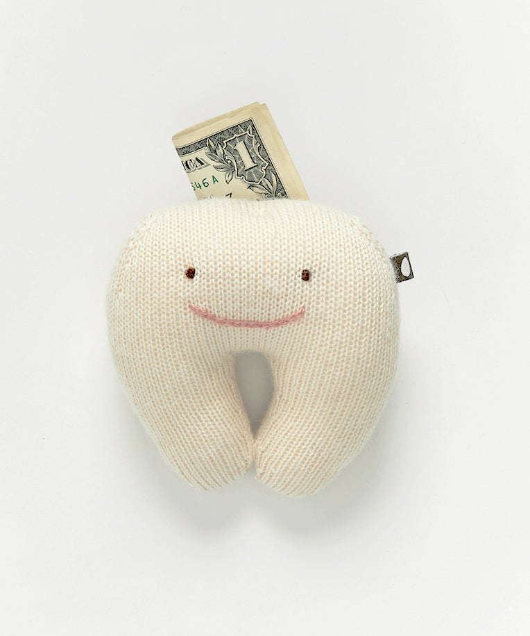 The Tooth Fairy Pillow, a plush smiling tooth toy, holds a folded dollar bill against a plain background.