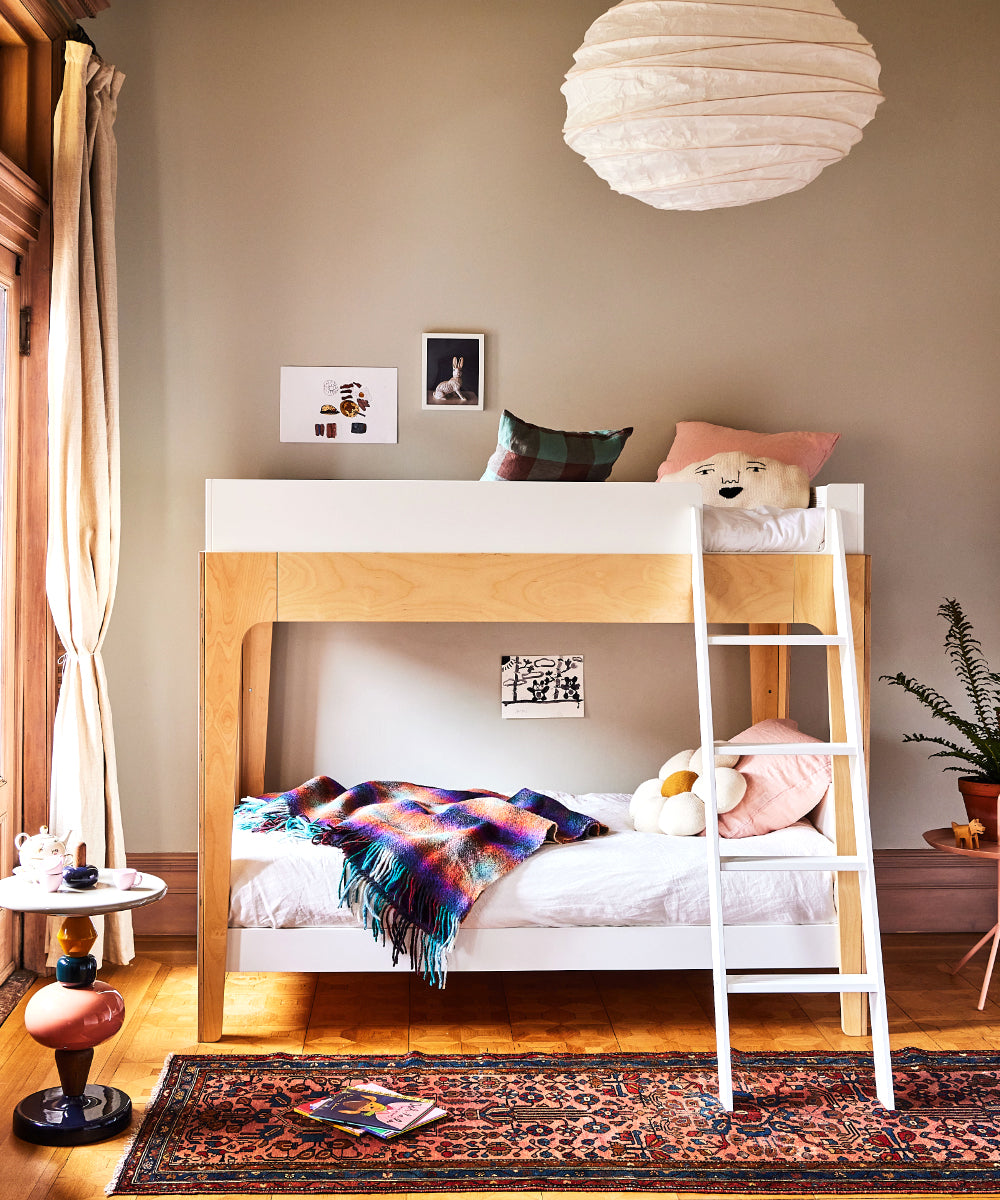 A cozy bedroom features a Perch Twin Bunk Bed, colorful pillows, and a bright knit blanket, all illuminated by a globe pendant light.