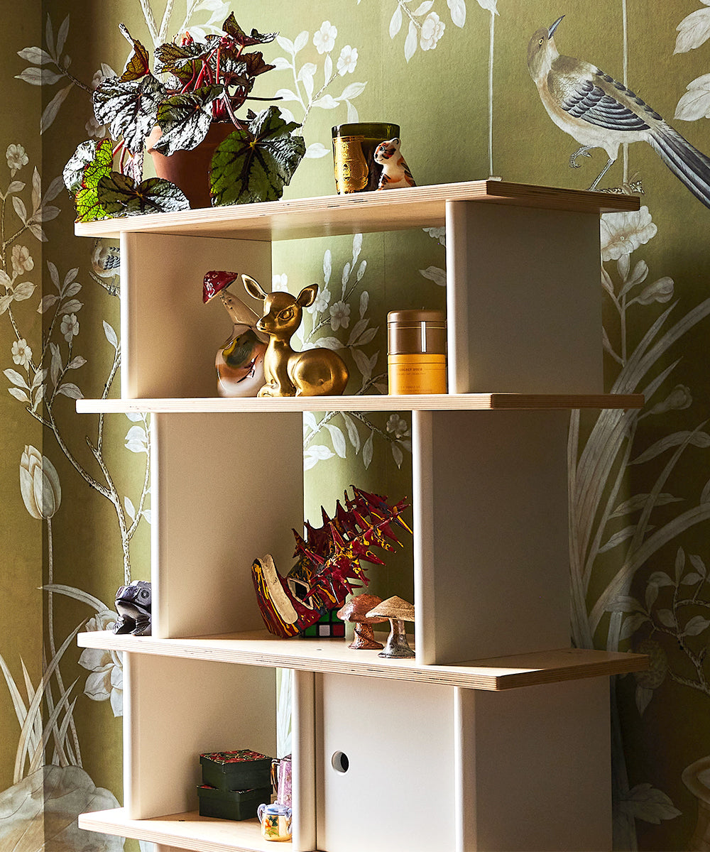 The Vertical Mini Library showcases plants, figurines, and jars against floral wallpaper with a bird design.